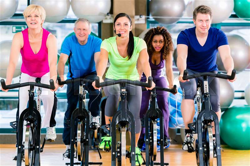 Fitness group of men and women spinning of bike in gym to gain strength and fitness, stock photo