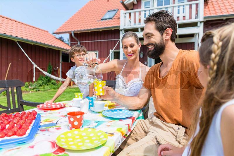Family drinking coffee and eating cake front of house, stock photo
