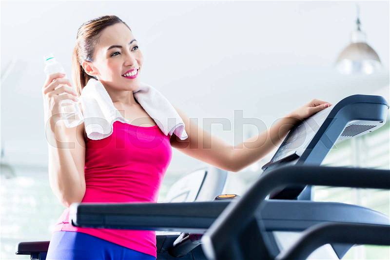 Smiling young woman on treadmill presenting water bottle as a reminder of sufficient hydration during workout, stock photo