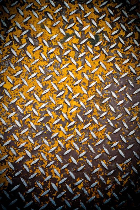 Close up of real diamond plate material with a slight vignette. Most of the yellow paint is chipped and scratched off, stock photo