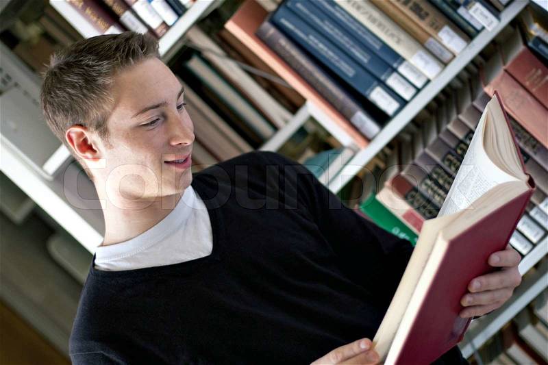 A young college aged man reading a book at the library, stock photo