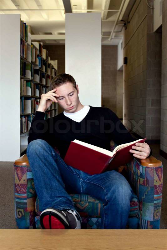 A young college aged man reading a book at the library, stock photo