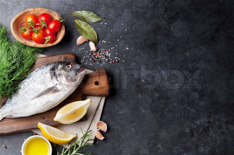 Raw fish cooking and ingredients. Dorado, lemon, herbs and spices. Top view with copy space on stone table, stock photo