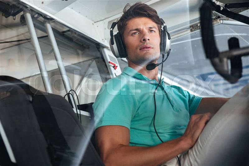 Portrait of serious young man pilot in cabin of private aircraft, stock photo