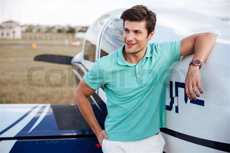 Happy handsome young man standing in field near small private airplane, stock photo