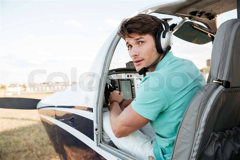 Attractive young man pilot sitting in cabin of small airplane, stock photo