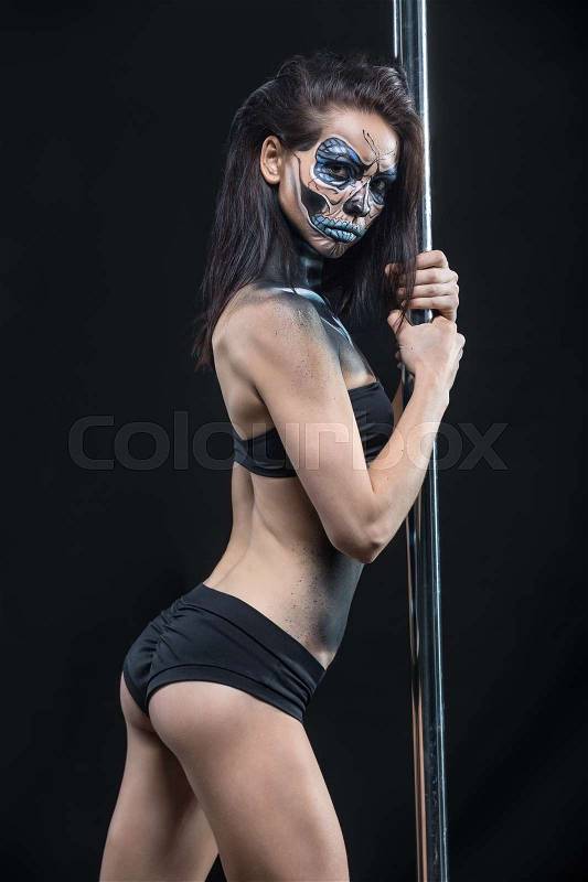 Hot pole dancer in black sport underwear holds her hands on the pylon in the studio on the dark background. She has a body-art on her body. Girl looks into the camera with a grimace. Vertical. , stock photo