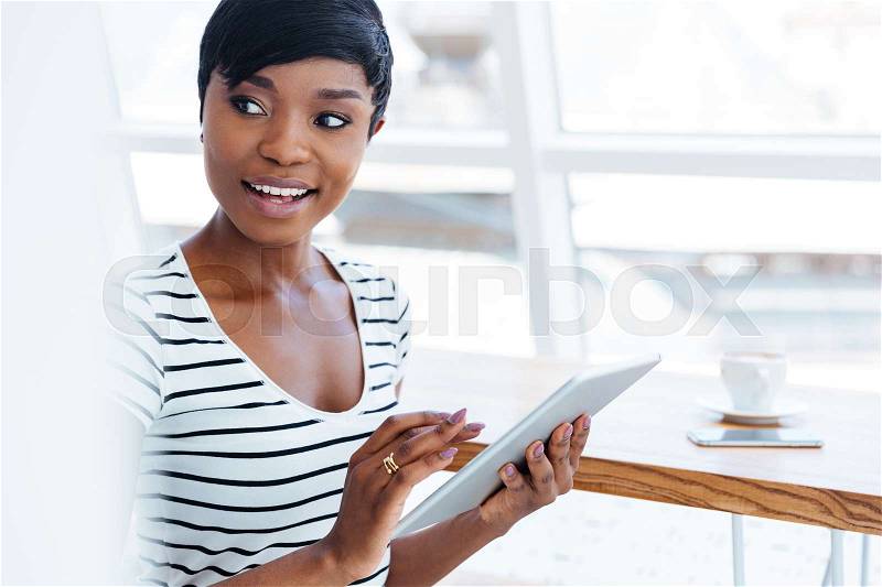 Attractive afro american businesswoman holding tablet computer and looking away in office, stock photo