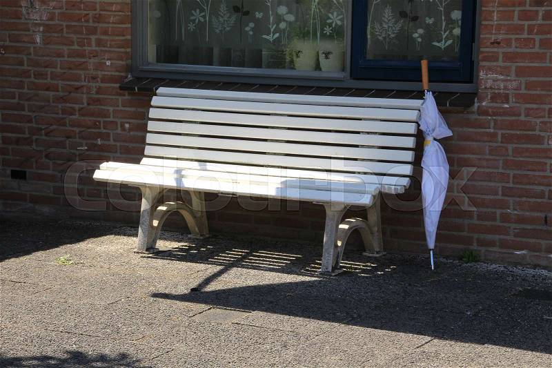 A white bench and an umbrella before the window of the house in the residential area in the village in the summer, stock photo