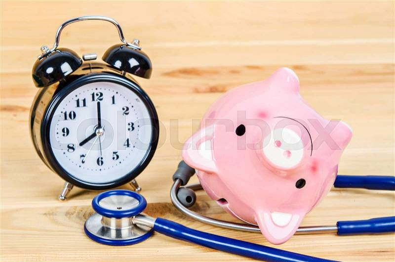 Pink piggy bank with stethoscope and alarm clock on wooden background, stock photo