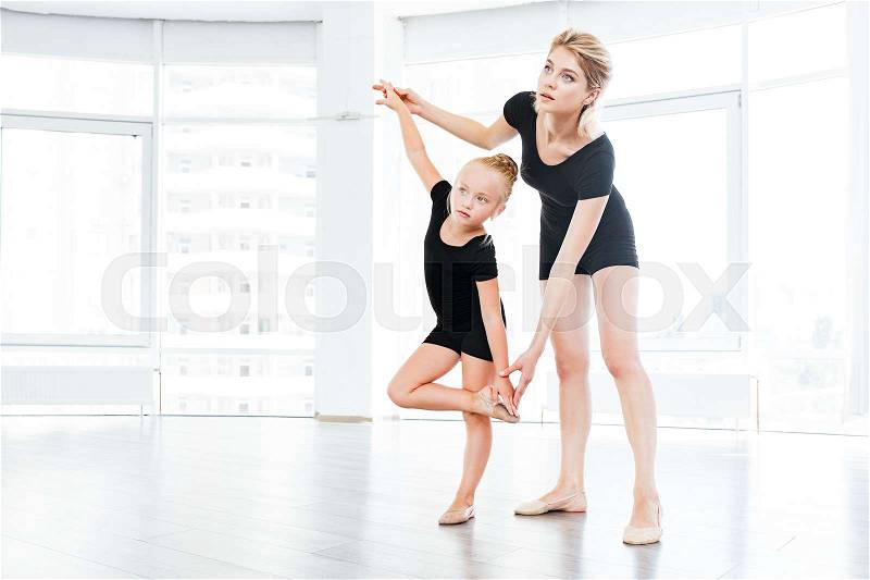 Young little girl ballerina learning dance lesson with female ballet teacher at studio, stock photo