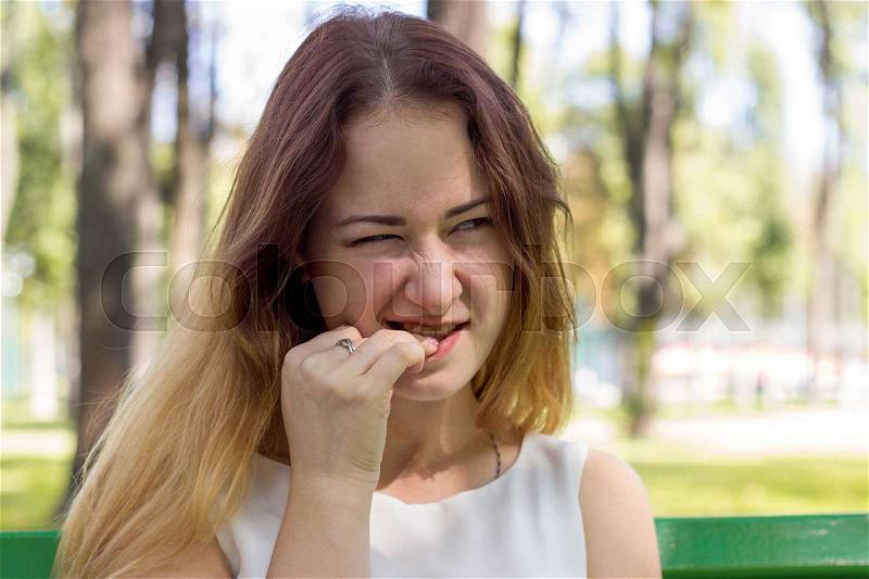 Young woman is biting her nails in the park, stock photo