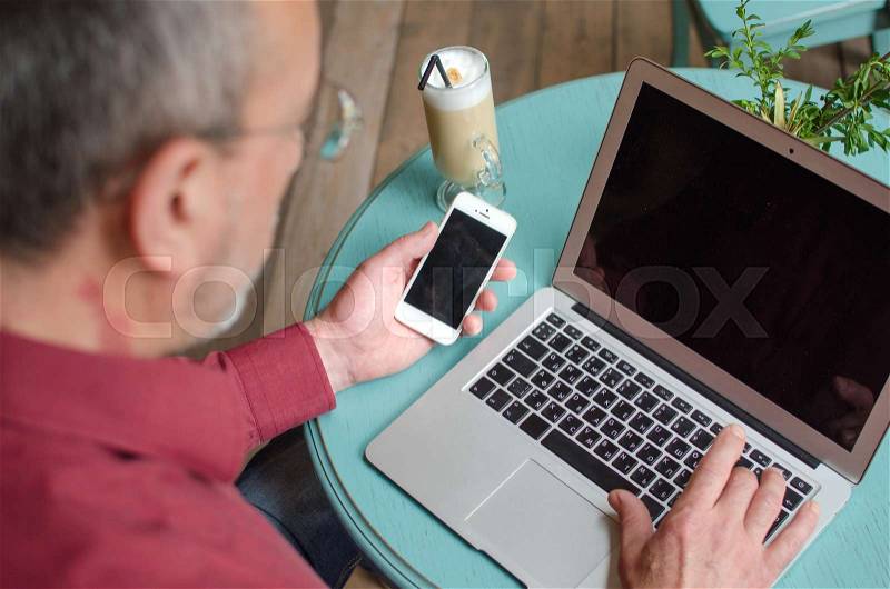 Aged man using his phone and lap top in the cafe, stock photo