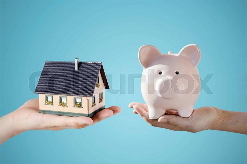 Hand holding house miniature and piggy bank. Home budget and finance concept, stock photo