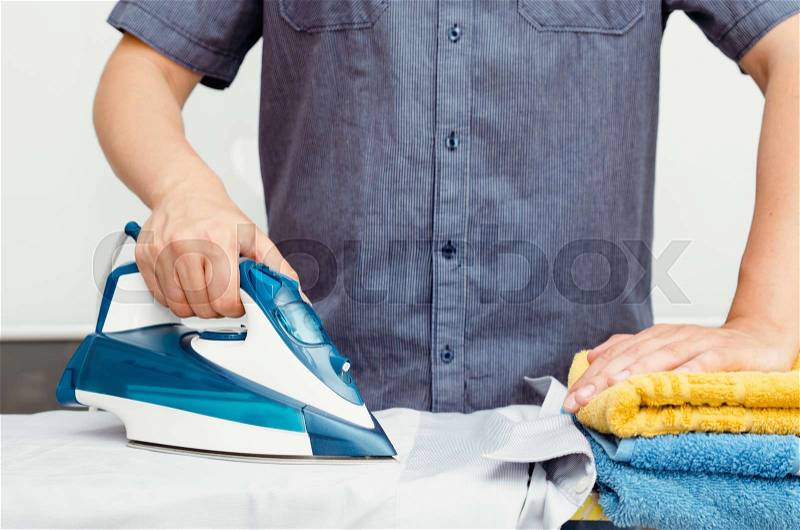 Man irons clothes on ironing board with steaming blue iron, stock photo
