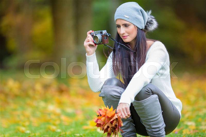 Young attractive brunette woman holding the retro camera in outdoors. Beautiful young girl shooting with retro camera in the autumn sunny day, stock photo
