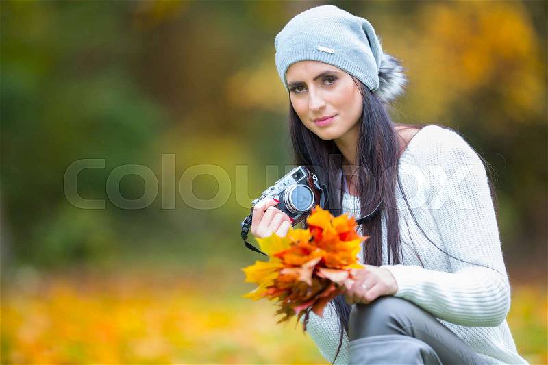 Young attractive brunette woman holding the retro camera in outdoors. Beautiful young girl shooting with retro camera in the autumn sunny day, stock photo
