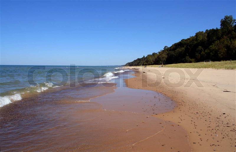 A generic beach background with sand, rolling waves and bright blue sky, stock photo