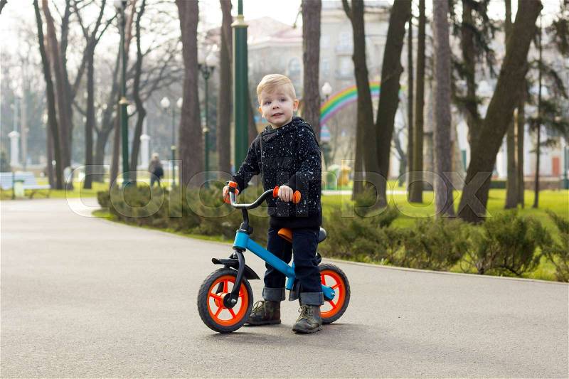 Little boy on the run bike is standing and looking forward in the park, stock photo