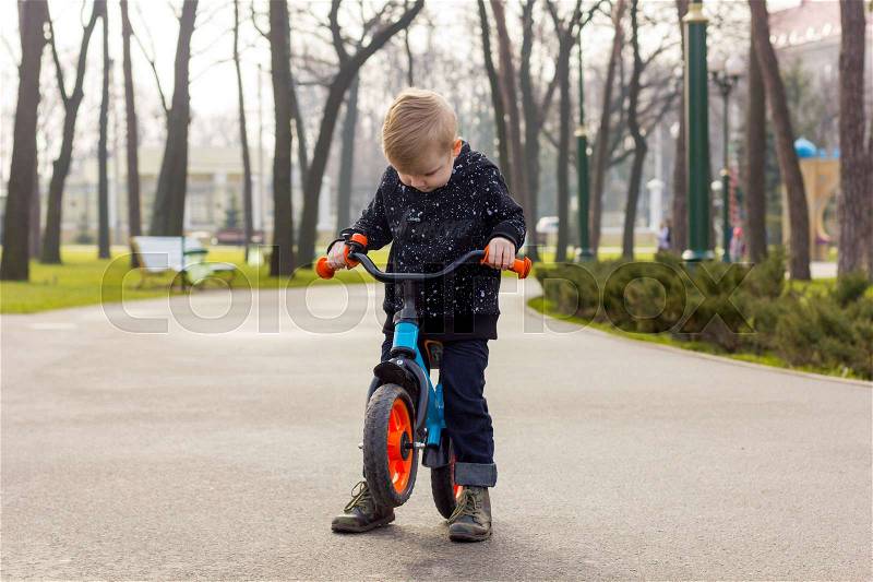 Little boy is picking up the run bike and looking down, stock photo