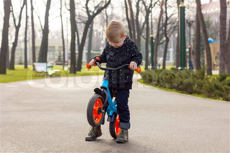 Little boy is picking up the run bike and looking down in the park, stock photo