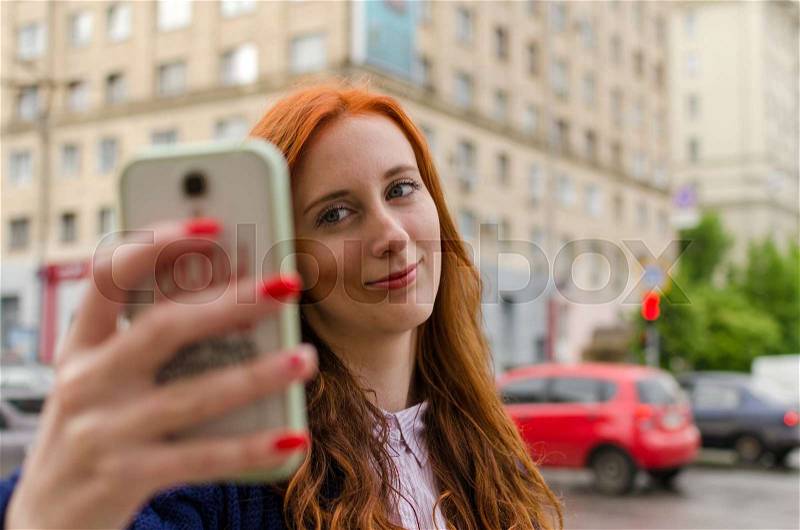 Young red woman making selfie with her cell phone, stock photo