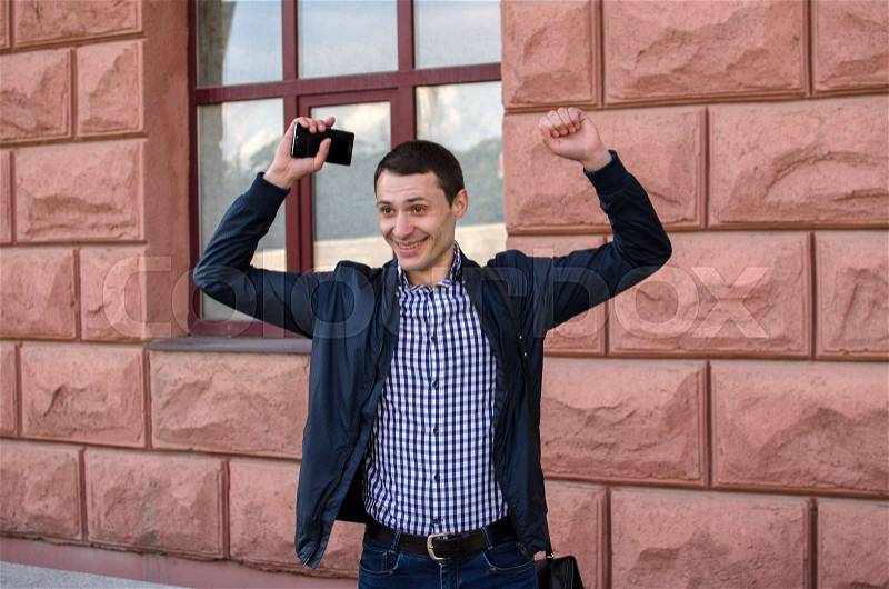 Happy young man with his hands up withthe building on the background, stock photo