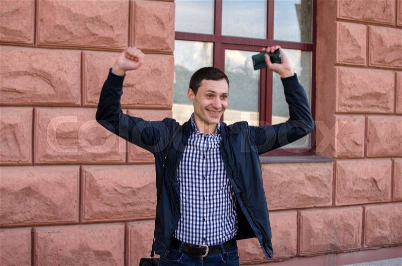 Happy young man with his hands up withthe building on the background, stock photo