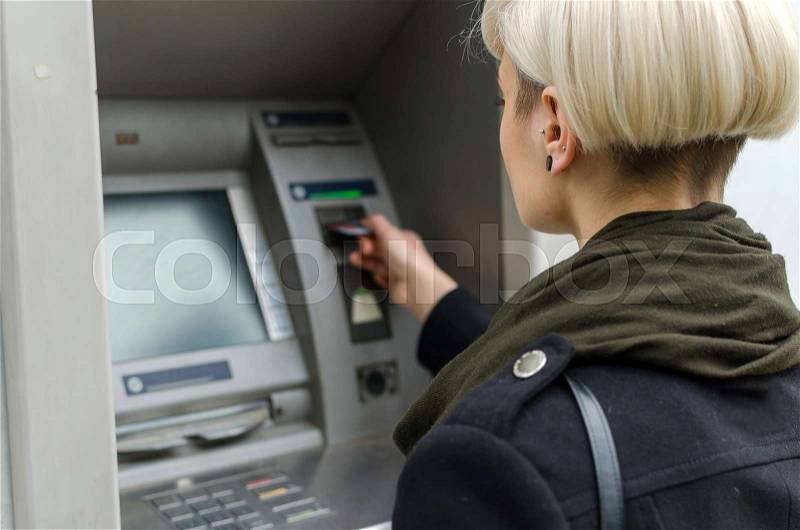 Young blonde woman using cash machine on the street, stock photo