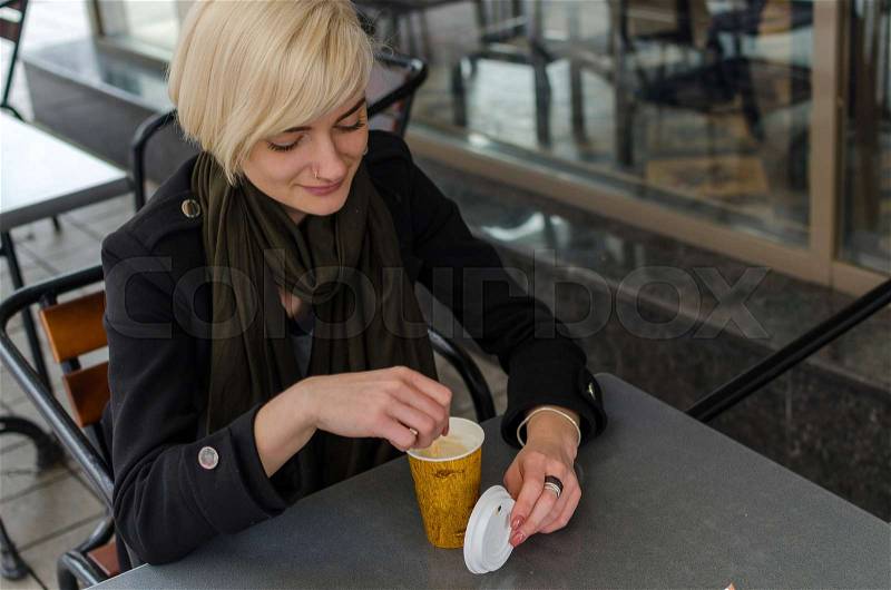 Young girl with a plastic cup of coffee walking on the cit streets, stock photo