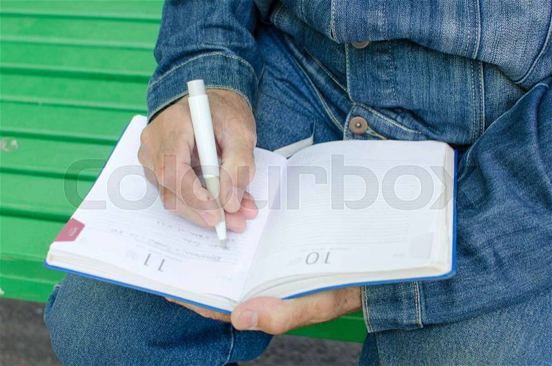 Aged man is making notes in the daily planner in the park, stock photo