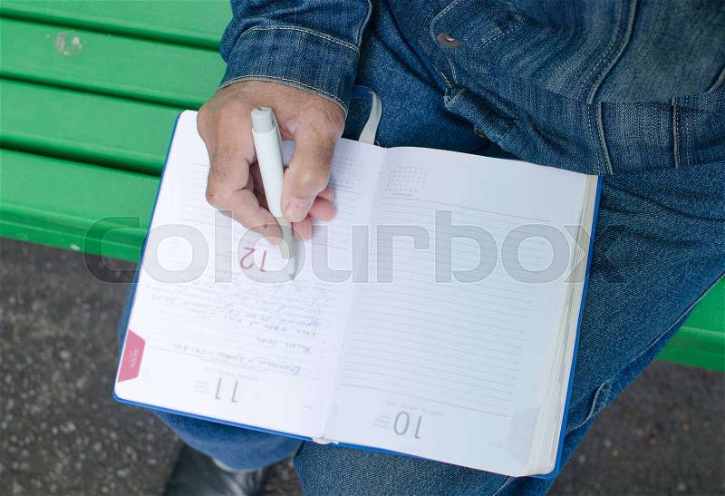 Aged man is making notes in the daily planner in the park, stock photo