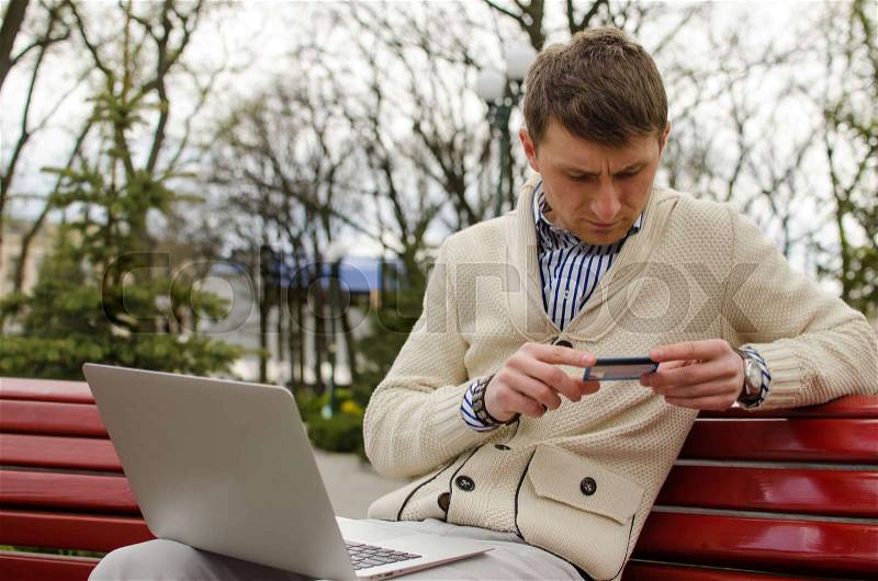 Young man is looking at credit card in the park, stock photo