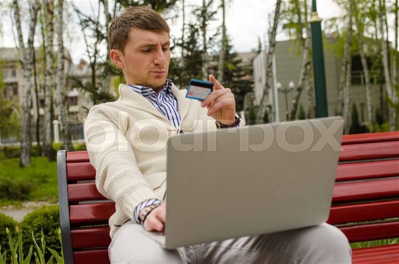 Serious man with laptop in park is looking at the card, stock photo