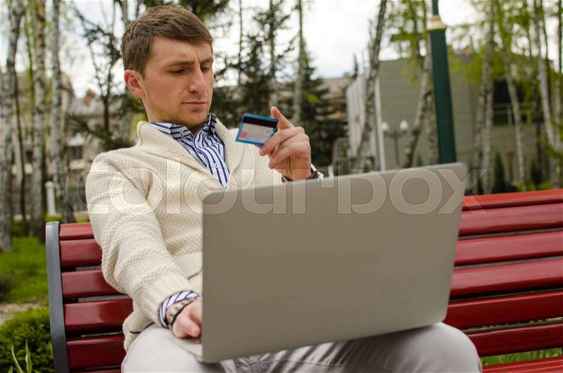 Serious man with laptop in park is looking at card, stock photo