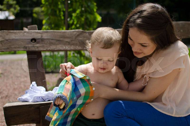 Young mother changes clothes for her small baby boy, stock photo