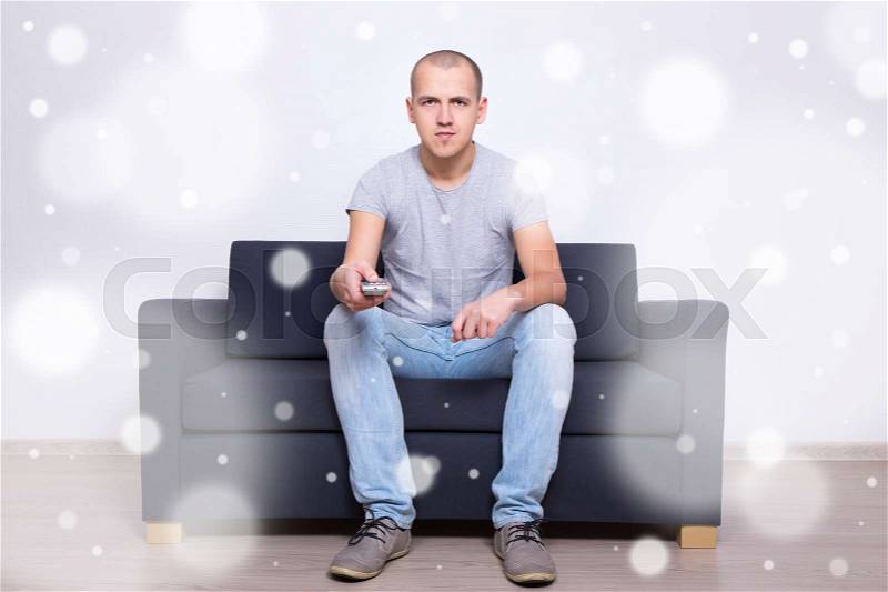 Young handsome man sitting on sofa and watching tv at home, stock photo