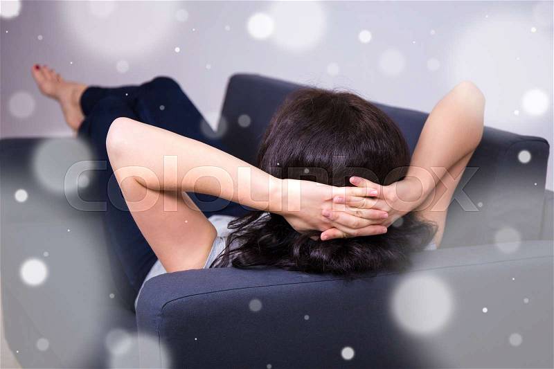 Back view of young woman lying on sofa at home, stock photo