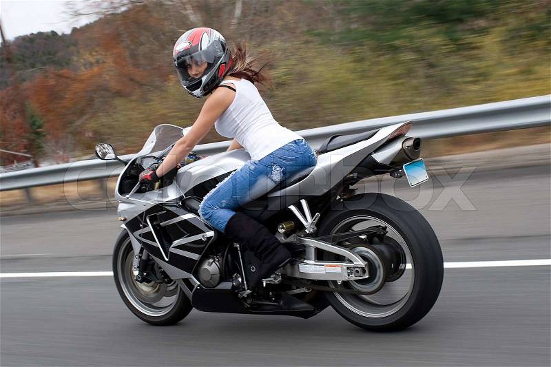 A pretty blonde girl in action driving a motorcycle at highway speeds, stock photo