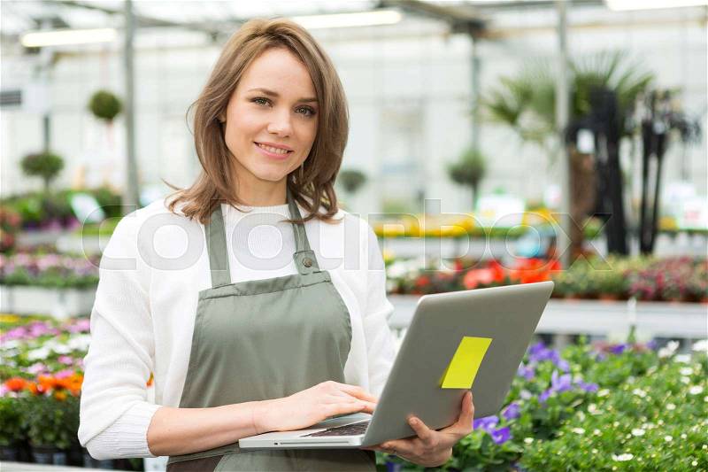 View of a Young attractive woman working at the plants nursery using laptop, stock photo