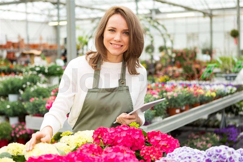 View of a Young attractive woman working at the plants nursery using tablet, stock photo