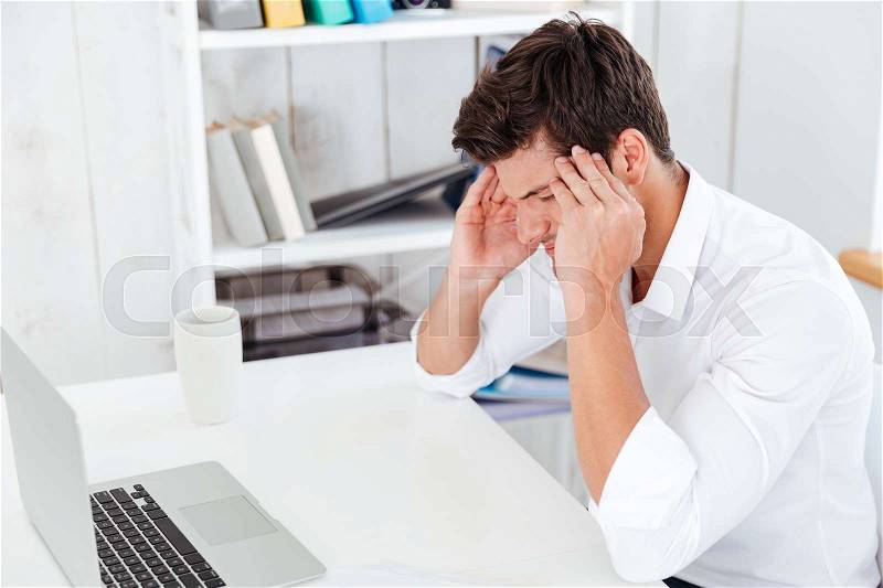 Stressed young businessman touching his temples and having a headache in office, stock photo