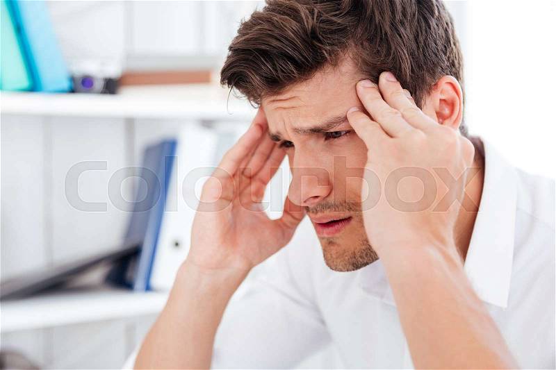 Close up portrait of a tired young businessman touching his temples and having a headache in office, stock photo
