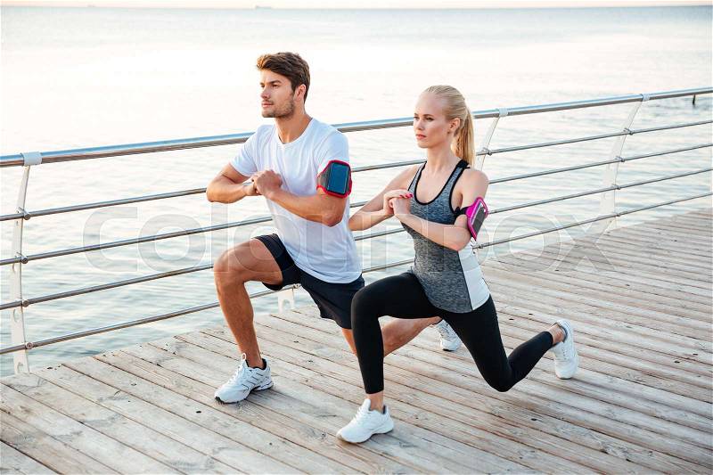 Athletic young couple sitting and stretching legs together on the pier, stock photo