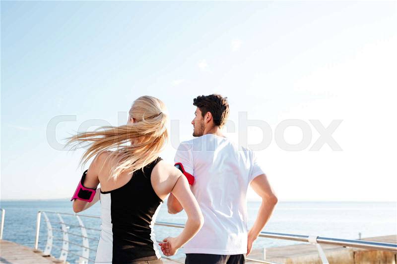 Back view of a couple exercising for marathon and workout fitness at the beach pier, stock photo