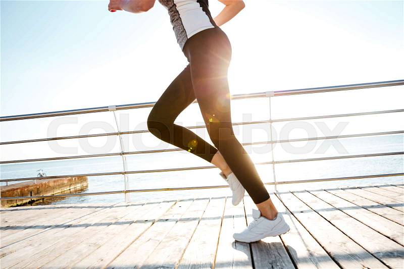 Cropped image of a runner woman feet in action at the wooden pier at sunrise, stock photo