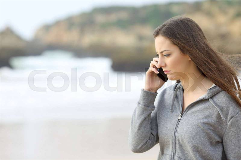 Sad teen talking on the phone on the beach, stock photo