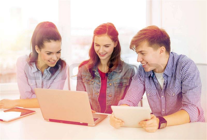 Education, technology, school and internet concept - three smiling students with laptop and tablet pc at school, stock photo