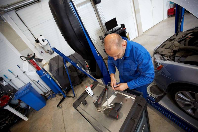 Car service, repair, maintenance and people concept - auto mechanic man with wrench and lamp working at workshop, stock photo