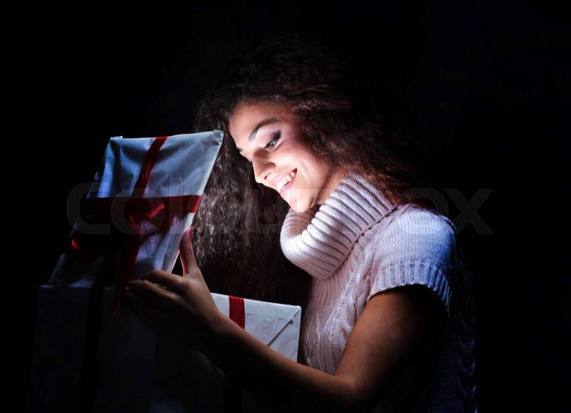 Excited cheerful attractive young woman opening gift over black background, stock photo